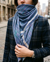 Load image into Gallery viewer, Blaues CHAYE Pashmina-Foulard mit heller Bordüre und feinen Karos, hoch um den Hals getragen zum dunklen karierten Sakko.