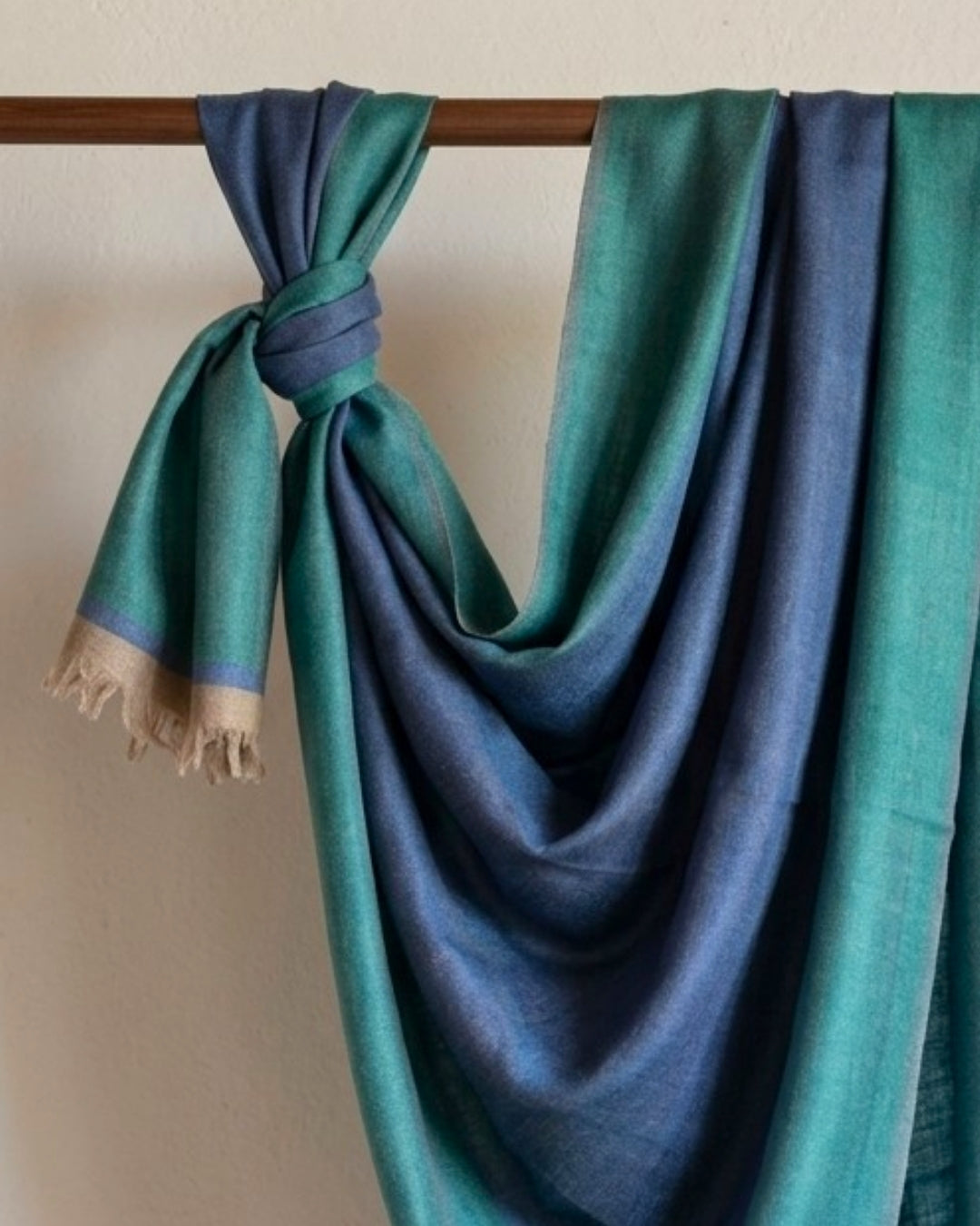 GURU Pashmina in Blau und Grün, links an einer Holzstange geknotet und in weichen Falten drapiert