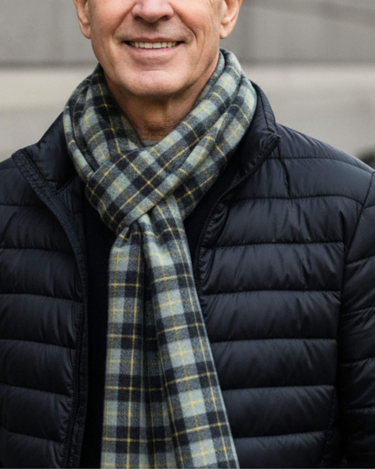 AJAX Kaschmir Schal mit blau-olivfarbenen Karos und gelben Linien, durch eine Schlaufe zur dunkelblauen Steppjacke getragen.