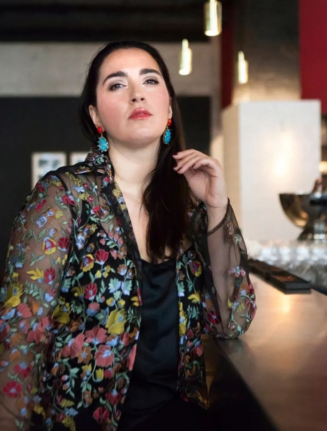 Model trägt AMARI Ohrringe mit orangefarbenen Steckern und türkisfarbenen Tropfen zu einer transparenten Blumenbluse.