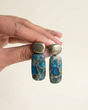 Charger l'image dans la visionneuse de la galerie, ANJA Ohrringe mit metallisch schimmernden Pyrit-Oberteilen und blauen Kupfer-Türkis-Anhängern mit goldfarbenen Adern, in einer Hand gehalten.
