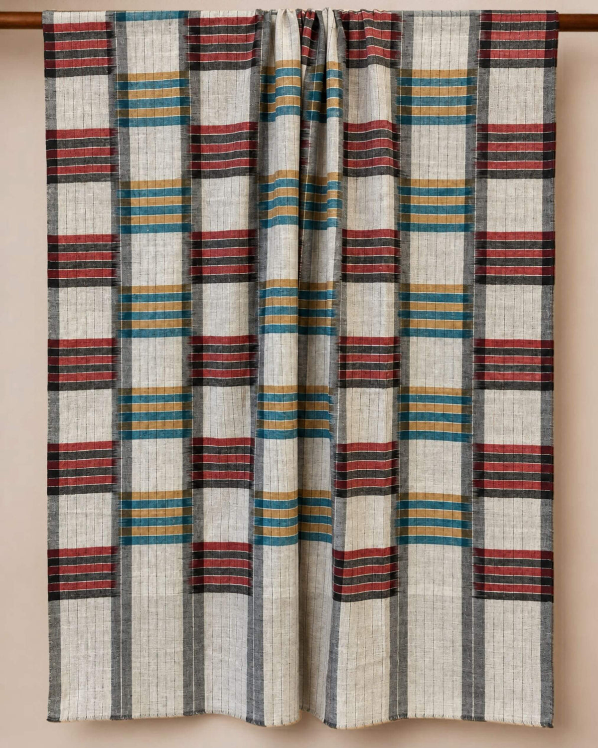ARLO Pashmina-Schal auf Creme mit grauen Linien und Streifenblöcken in Rot, Petrol und Ocker, über eine Stange gelegt.