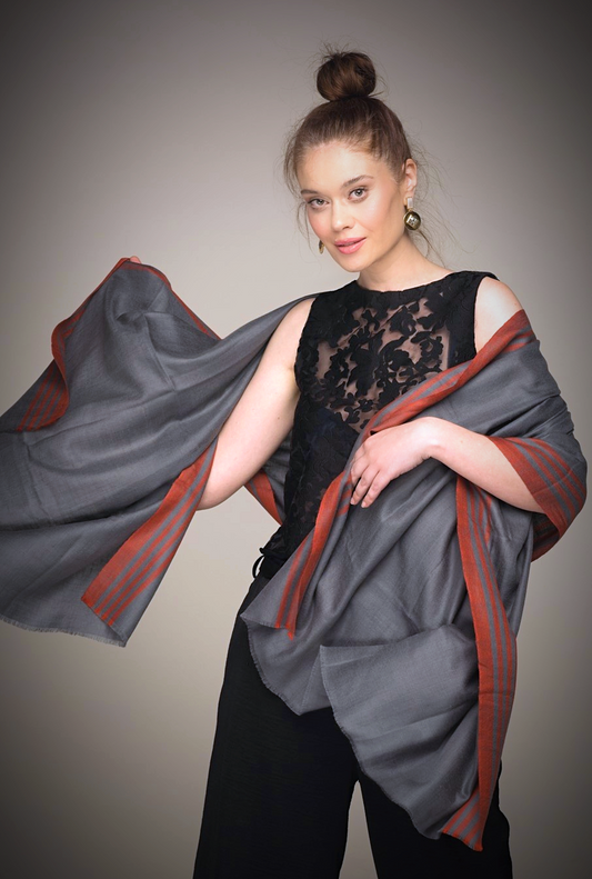 ERUS Pashmina aus Ladakhi Kaschmir in Graublau mit roter Streifenborde, über die Schultern zu einem schwarzen Outfit gelegt.