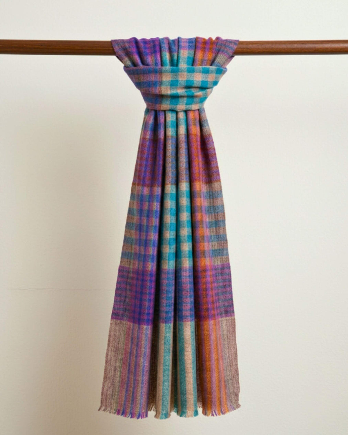 FEZZ Pashmina-Schal als Schlaufe um eine Holzstange, mit bunten Karos und langen, gefransten Enden.
