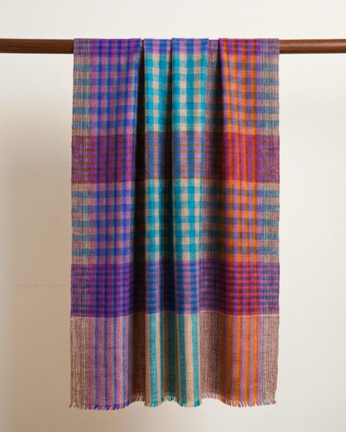 FEZZ Pashmina-Schal über einer Holzstange, mit türkis-violettem Karomuster und feinen Fransen.