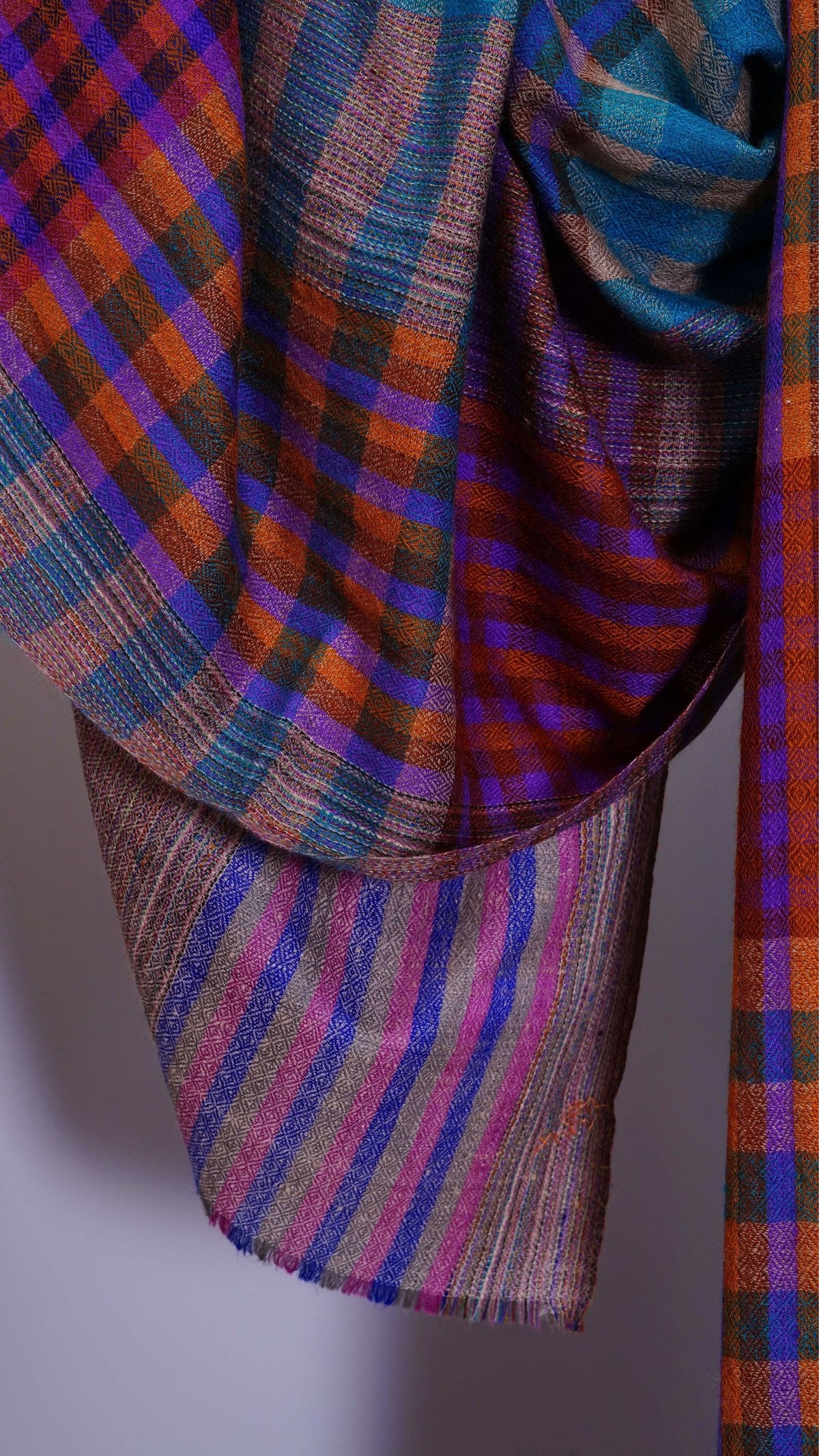 Nahaufnahme des FEZZ Pashmina-Schals mit feiner Webstruktur, Karos und Streifen in Türkis, Violett und Orange.