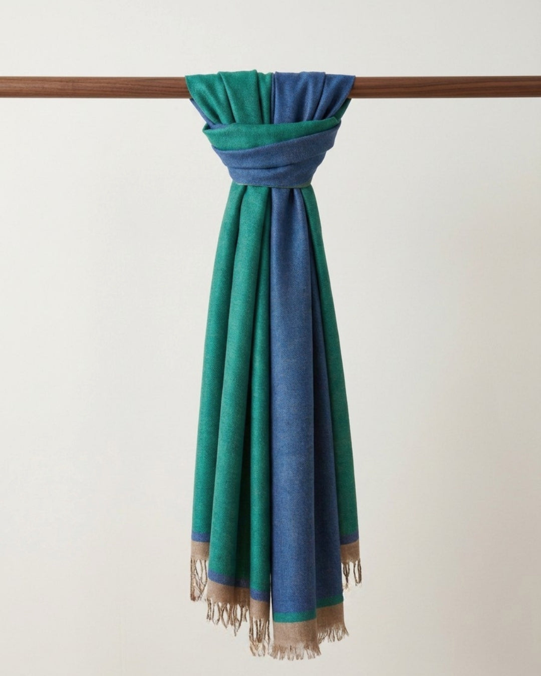 GURU Kaschmir Schal in Grün und Blau mit beiger Fransenborde, locker um eine Holzstange geknotet.