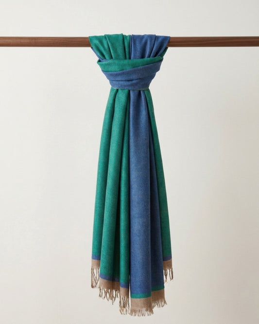 GURU Kaschmir Schal in Grün und Blau mit beiger Fransenborde, locker um eine Holzstange geknotet.