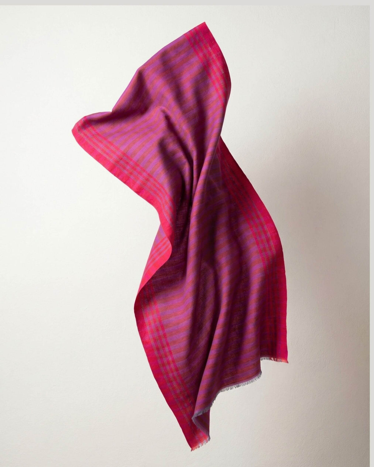 HARI Pashmina in geschwungener Form vor hellem Hintergrund, mit pink-orangen Streifen und violetten Nuancen.