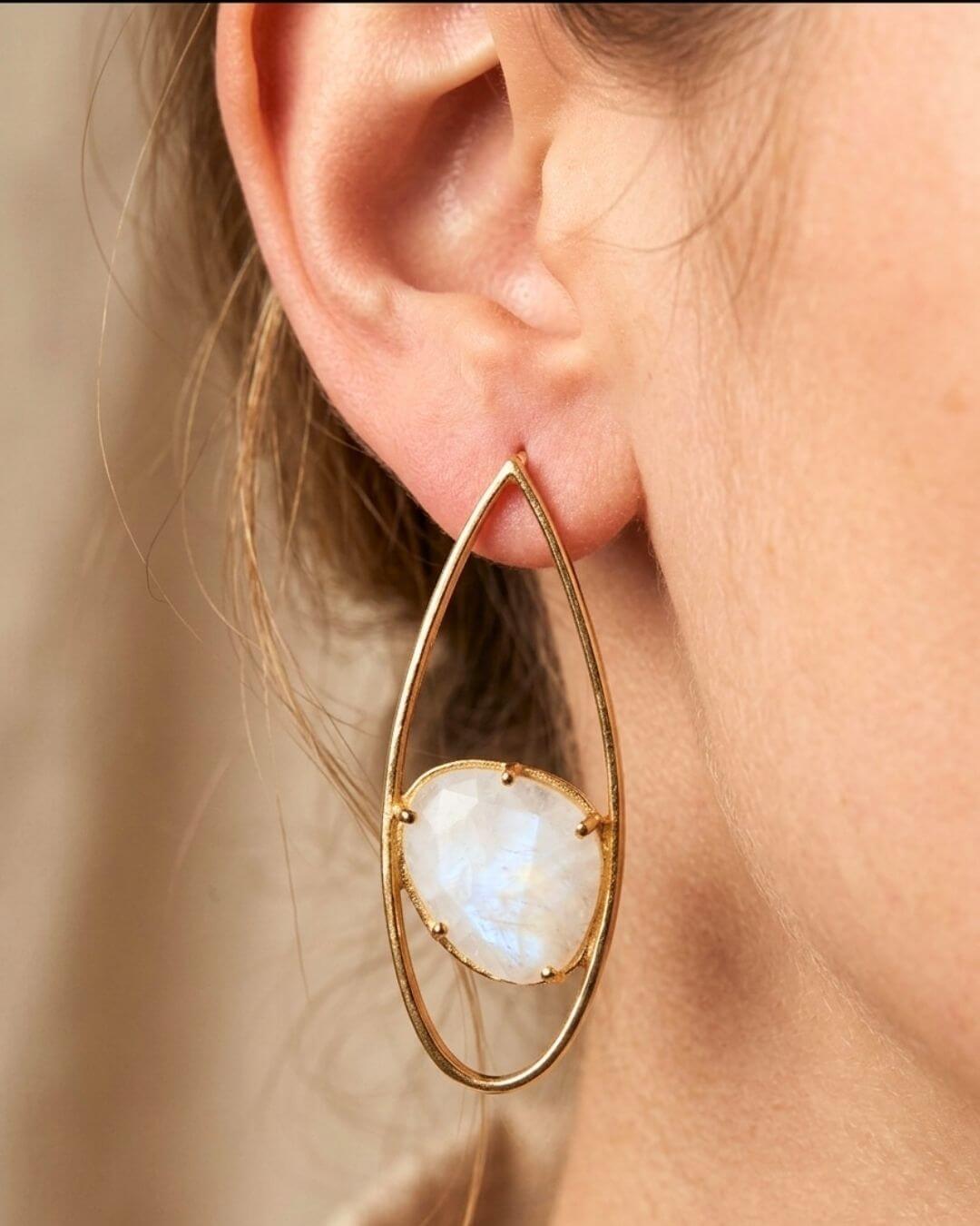 Nahaufnahme eines getragenen INDU Ohrrings mit hellem Mondstein in goldfarbener Tropfenform.