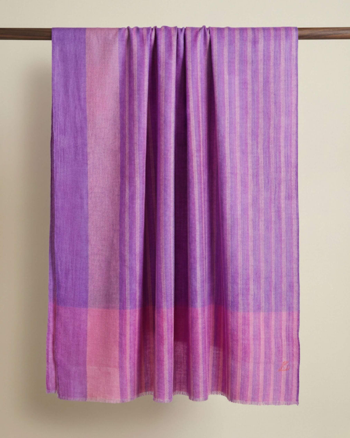 LILOU Pashmina-Schal in Flieder und Rosé mit feinen Streifen, längs über eine Holzstange gelegt.