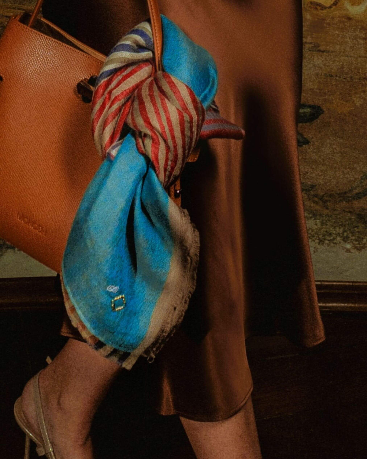 LYRIC Pashmina mit Streifen und türkisfarbenen Enden, an einer braunen Ledertasche zu einem dunklen Outfit getragen
