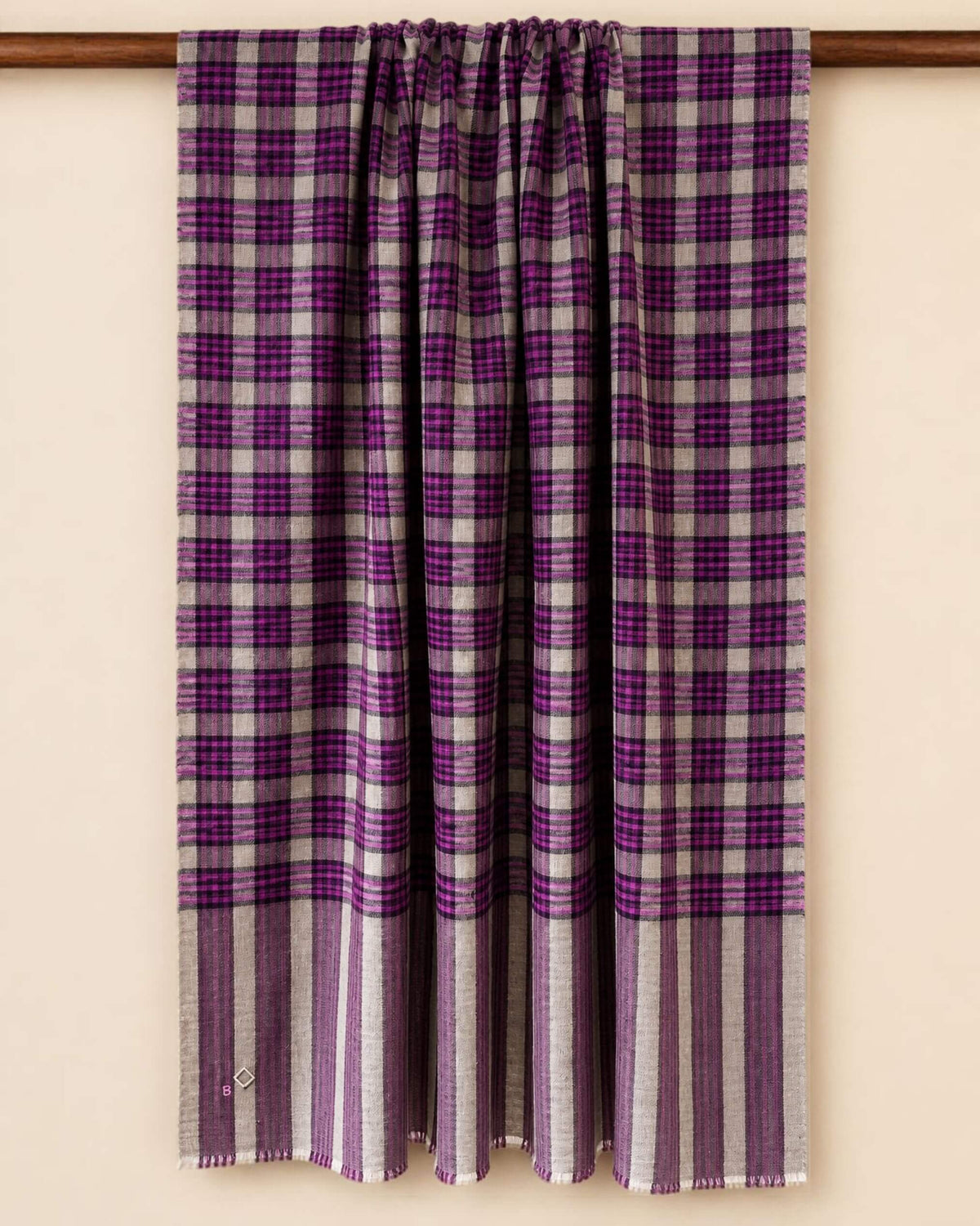 MORIX Pashmina-Schal über einer Holzstange, mit Karos in Beige, Magenta und Violett und gestreiften Enden.