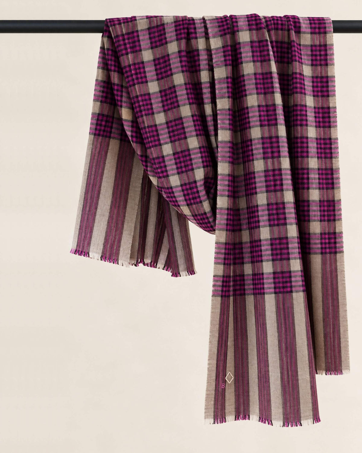 MORIX Pashmina-Schal locker über eine dunkle Stange drapiert, mit magentafarbenen Karos und beigen Streifen.