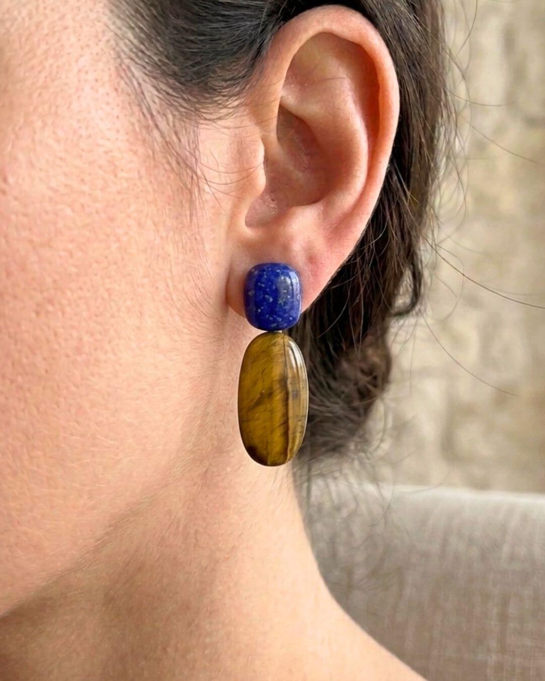 Seitliche Trageansicht eines PRIYA Ohrrings mit tiefblauem Lapislazuli und ovalem Tigerauge bei zurückgebundenem Haar.

