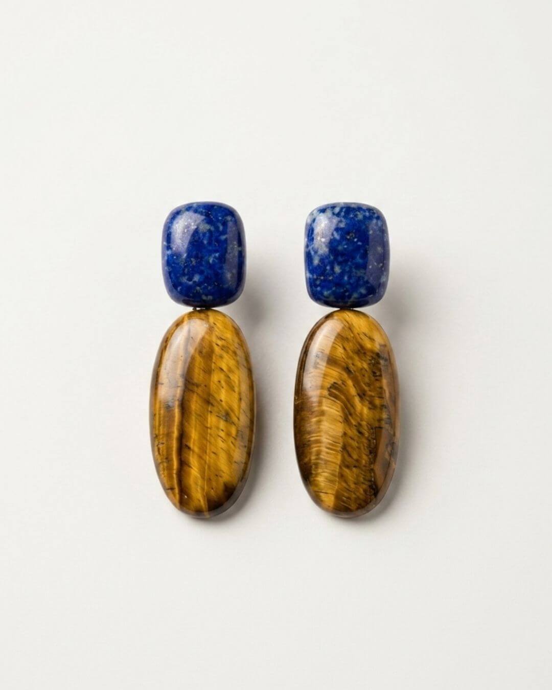 PRIYA Ohrringe mit tiefblauen Lapislazuli-Oberteilen und ovalen goldbraunen Tigerauge-Anhängern auf hellem Hintergrund.