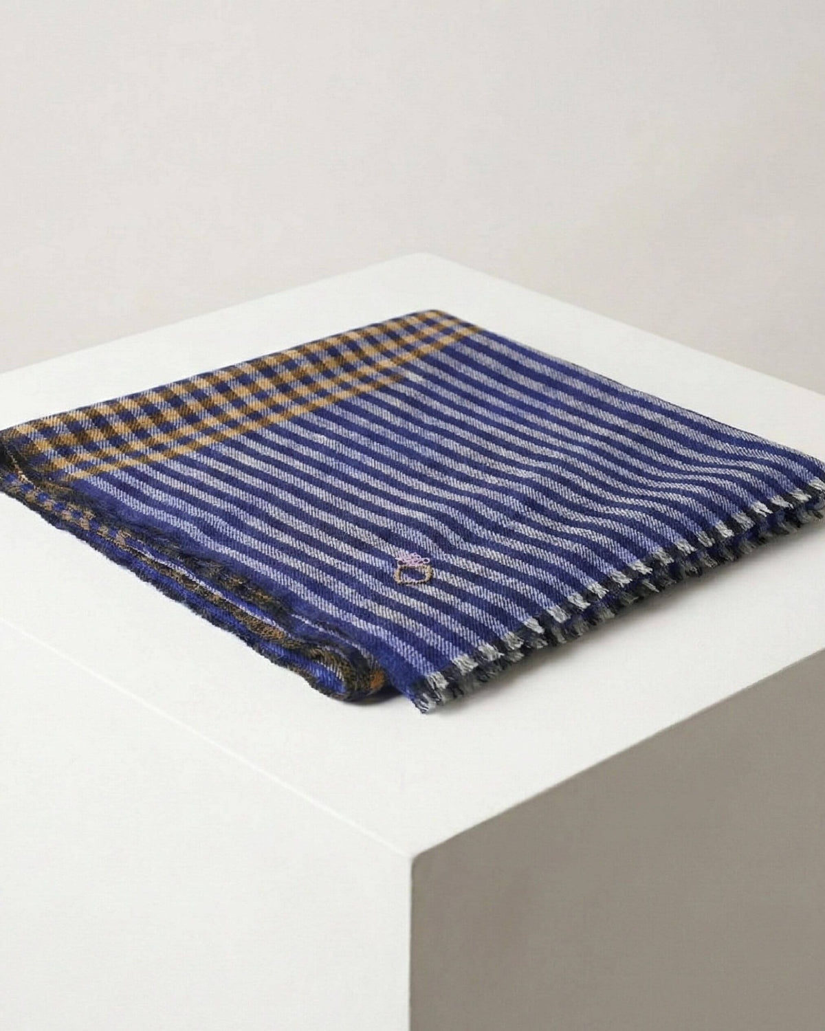 SAMM Pashmina-Schal gefaltet auf weissem Podest, mit blauen Streifen, senfgelben Karos und kurzen Fransen.