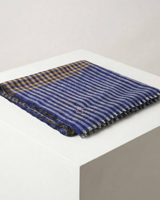 SAMM Pashmina-Schal gefaltet auf weissem Podest, mit blauen Streifen, senfgelben Karos und kurzen Fransen.