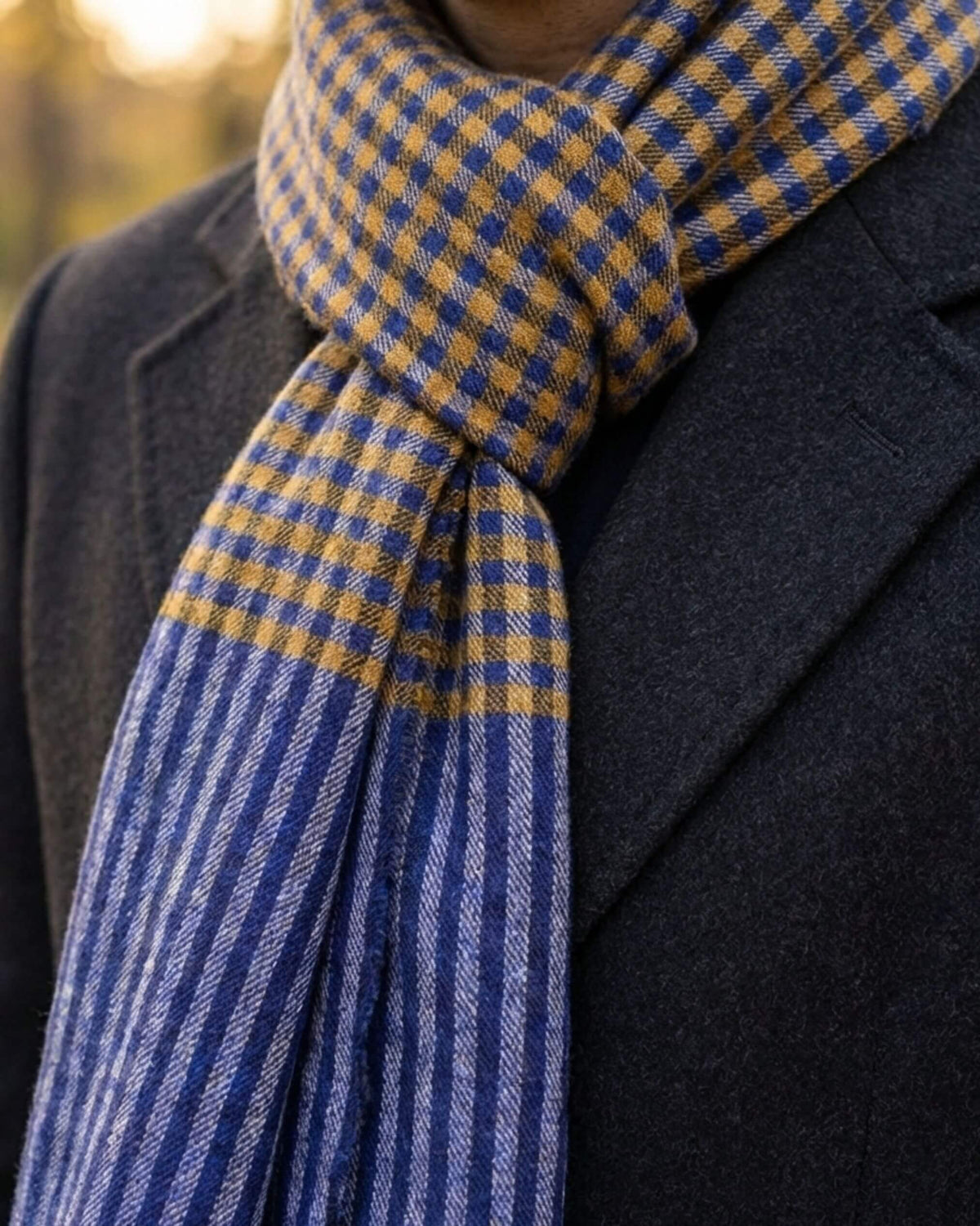 SAMM Pashmina-Schal zum dunklen Mantel geknotet, mit blau-senfgelben Karos und gestreiften Enden.