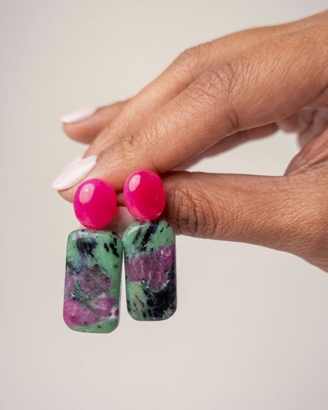 ZIVA Ohrringe mit leuchtend fuchsiafarbenem Chalcedon und grün-violett-schwarz gemustertem Rubin-Zoisit, in einer Hand gehalten.